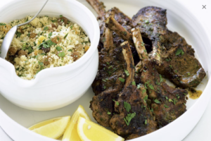 Moroccan braised lamb shank with couscous on a white plate with lemon garnishes